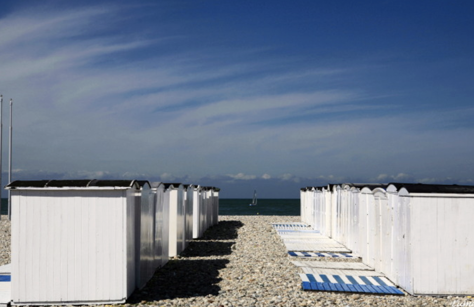 Cabanes de plage blanches alignées sur les galets de la plage du Havre face à la mer